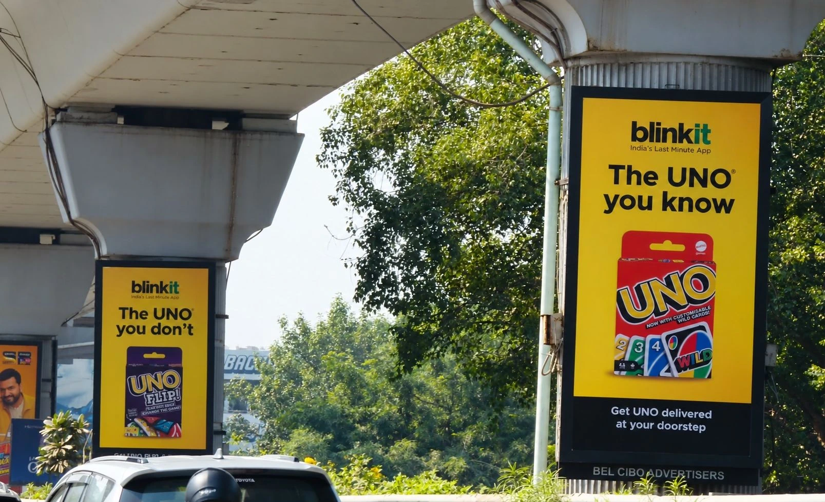 Two Blinkit and UNO ads installed on metro pillars along an elevated transit corridor.