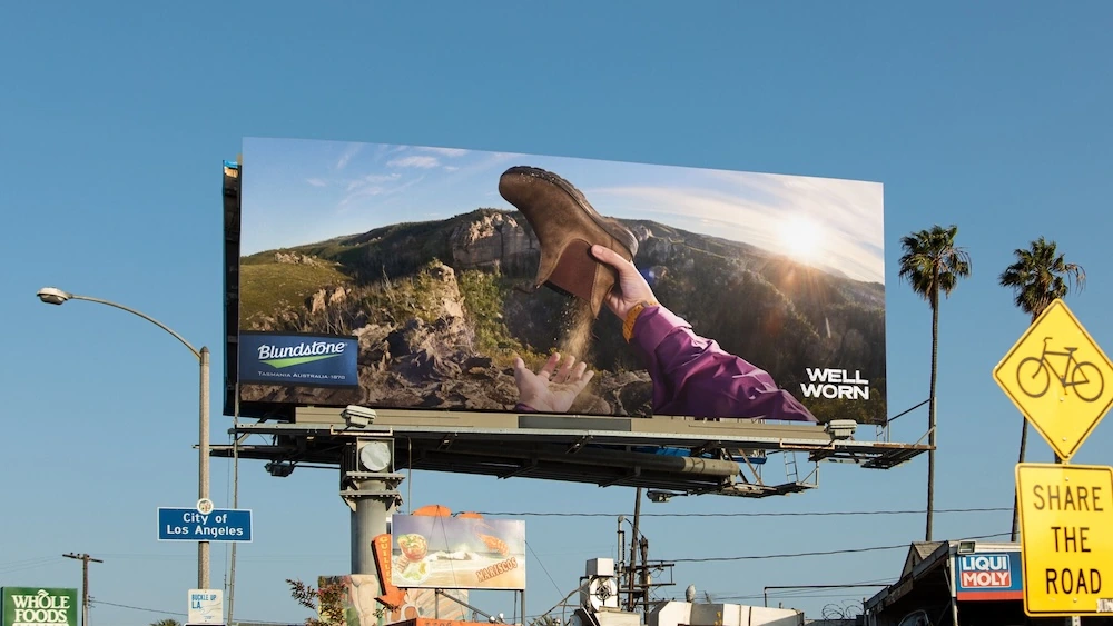 Blundstone Well Worn billboard in Los Angeles showing a worn brown boot held up against a rugged mountain landscape.