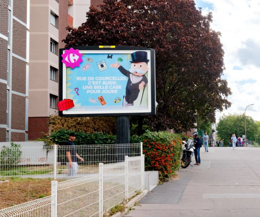 Carrefour Monopoly billboard on Rue de Courcelles in Paris featuring Monsieur Monopoly and the line 'Rue de Courcelles, c'est aussi une belle case pour jouer'.
