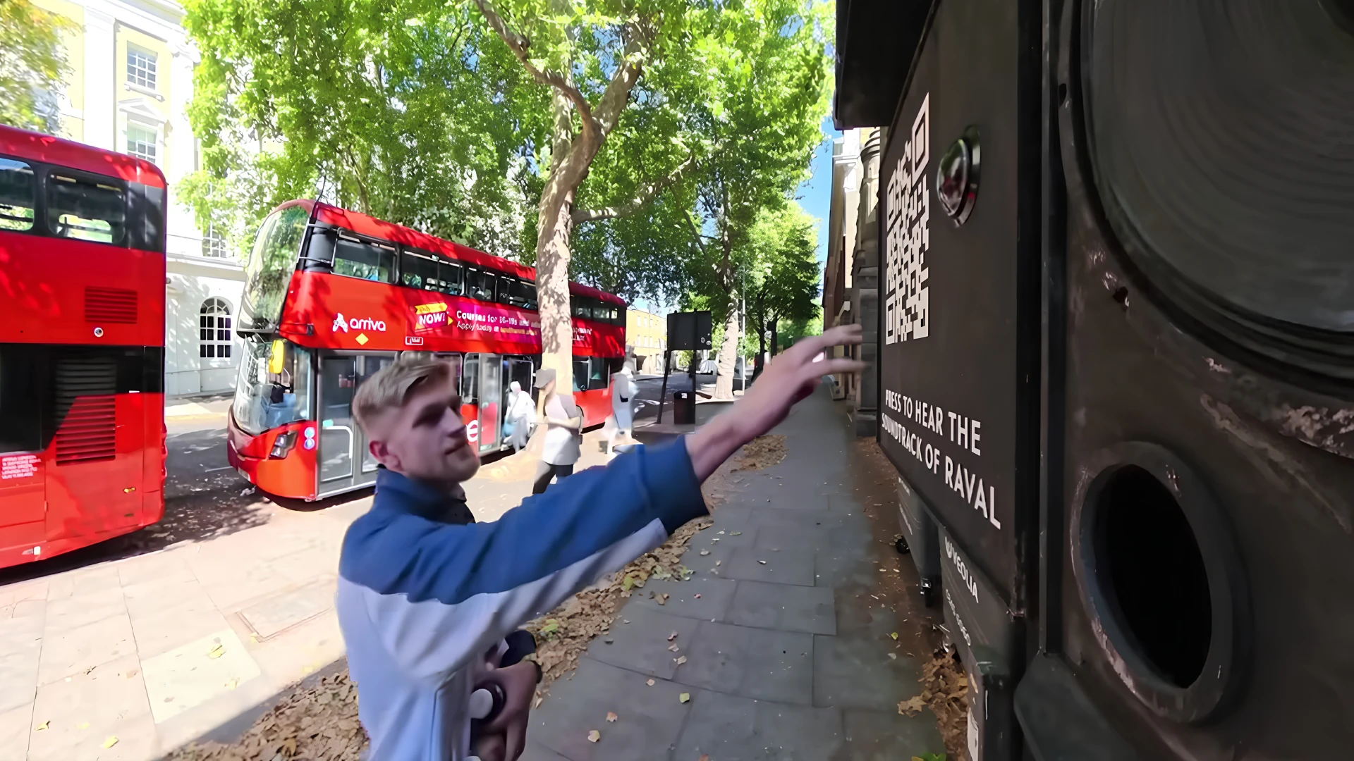 A passer-by reaches toward the interactive CUPRA Raval billboard beside a large built-in speaker and QR code while London buses pass in the background.
