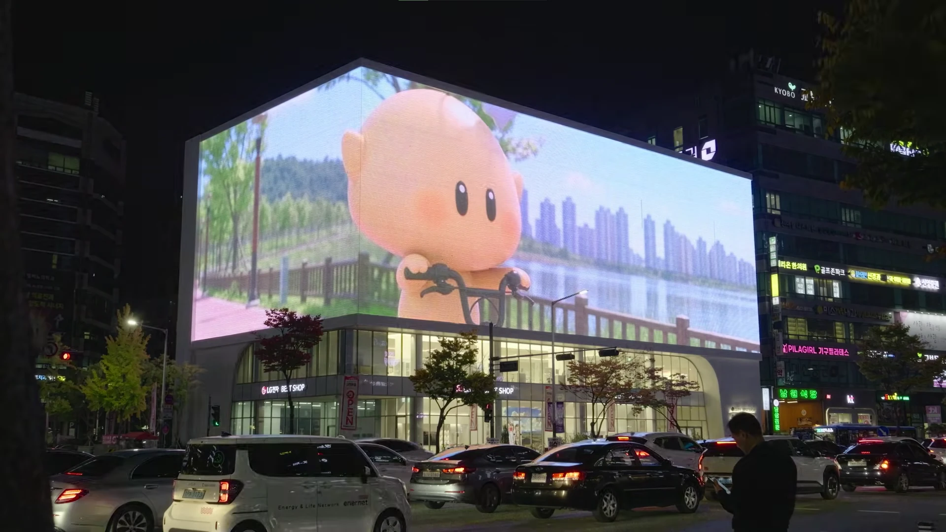 Large corner DOOH media wall in Dunsan-dong, Daejeon showing Kkumdori riding a bicycle in the AI-generated Letters from 2050 campaign.
