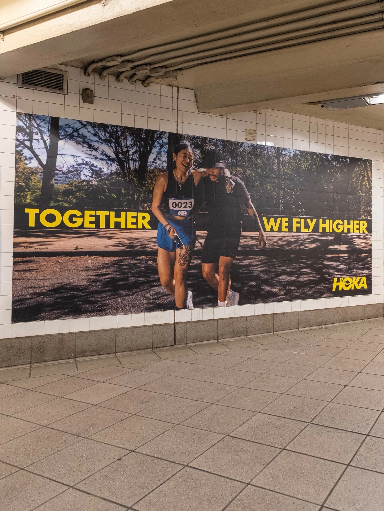 HOKA Together We Fly Higher subway OOH campaign showing runners supporting each other inside a New York transit station.