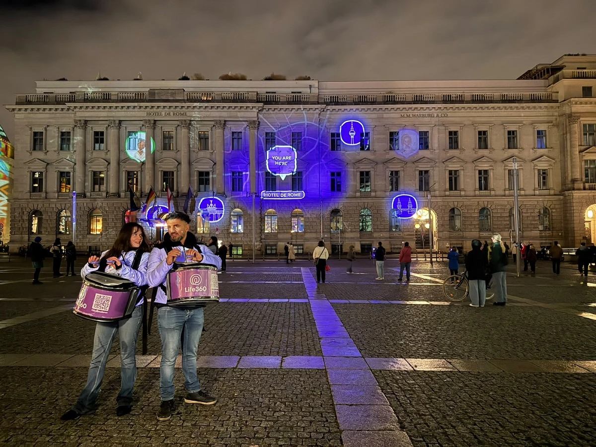 Life360 Routes of Love projection on Hotel de Rome in Berlin with glowing map routes, location icons and festival visitors in the foreground.