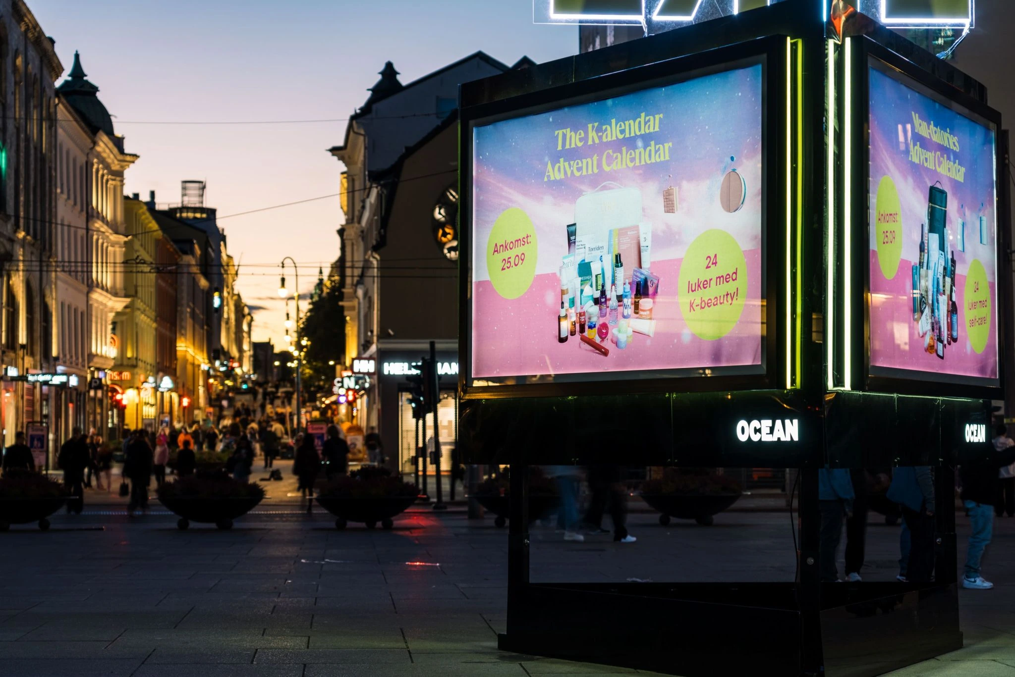 Close-up evening view of LYKO's Trinity special build in Oslo, with multiple digital faces displaying The K-alendar Advent Calendar creative and product imagery against the Jernbanetorget streetscape.