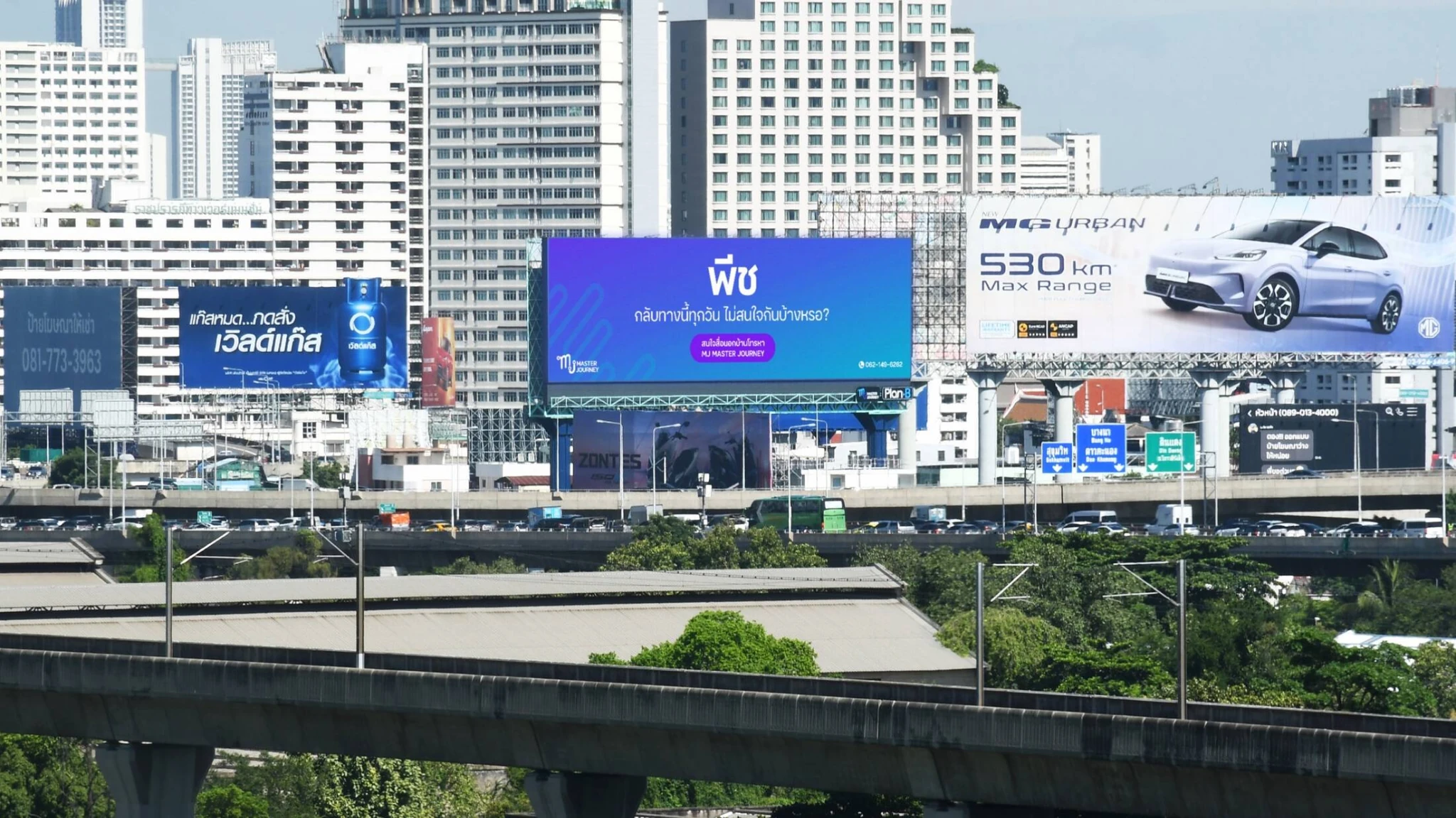 A Bangkok skyline view featuring multiple large-format roadside billboards, including MJ Master Journey's blue One Eyeball Billboard creative displayed prominently above a busy urban roadway.