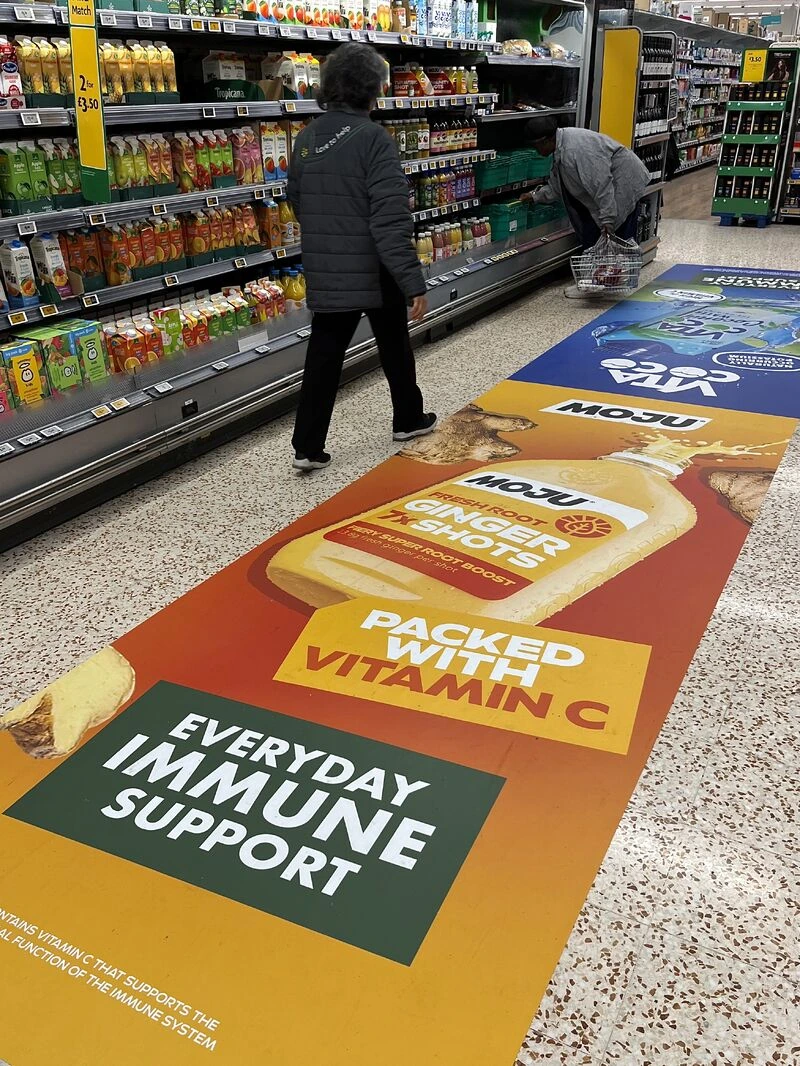 MOJU and Vita Coco full aisle takeover inside Morrisons featuring large floor graphics promoting ginger shots, hydration and everyday immune support.