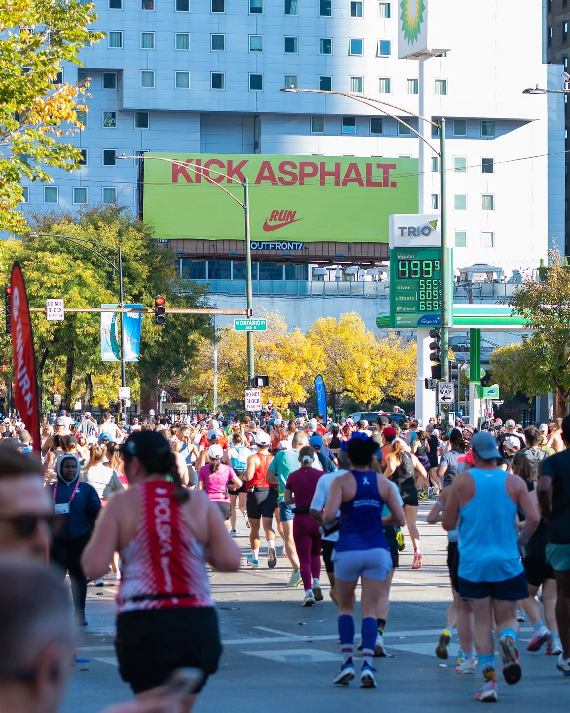Nike Running billboard along the Chicago Marathon route reading Kick Asphalt as runners pass below.