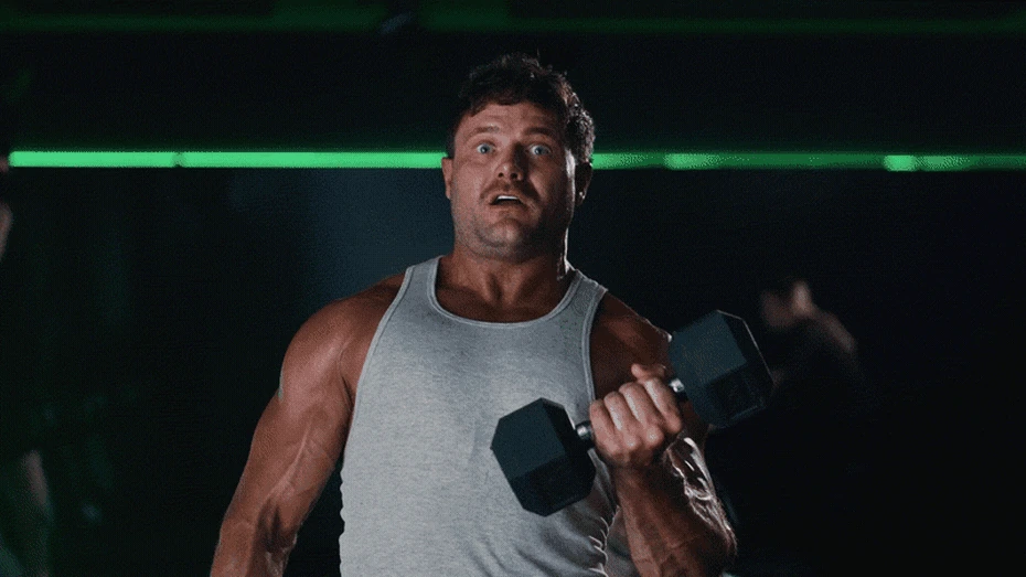 Planet Fitness Lunks campaign scene showing a muscular man lifting a dumbbell in a dark gym.