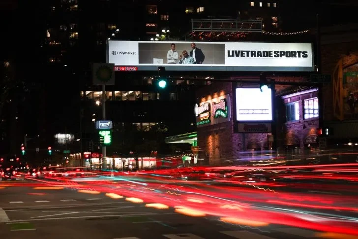 LIVETRADE SPORTS billboard by Red Star Outdoor above a busy Chicago intersection at night with light trails from traffic.