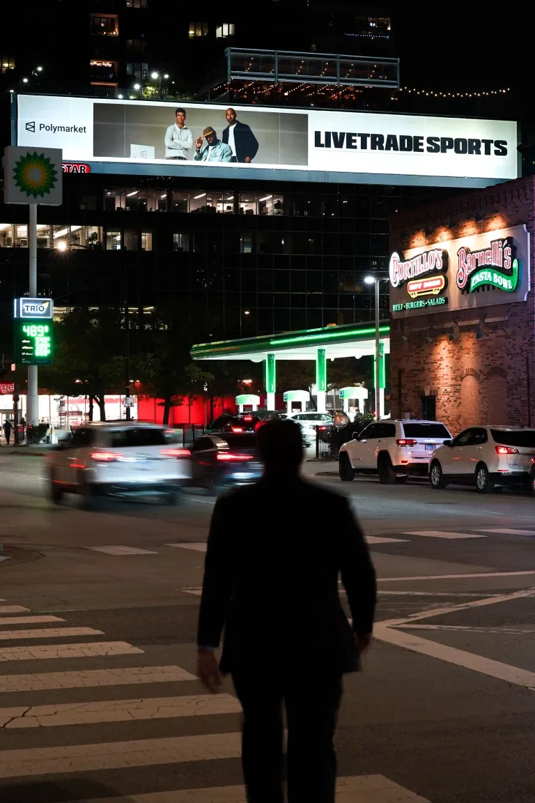 Red Star Outdoor LIVETRADE SPORTS billboard illuminated at night above moving Chicago traffic near restaurants and city lights.