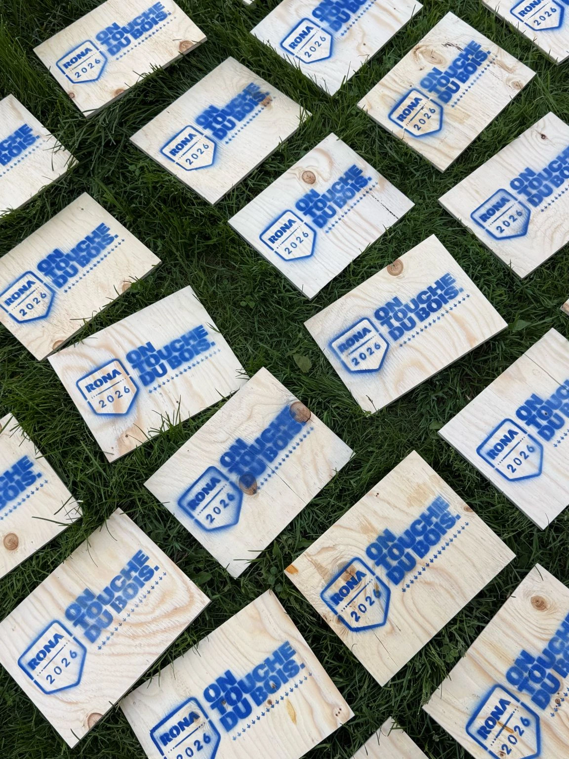 RONA campaign wood boards printed with the message On touche du bois laid out across grass.