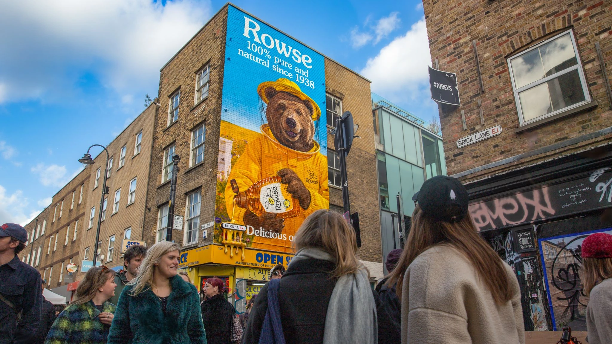 People walking past the Rowse honey wall mural near Brick Lane and Bacon Street in London.
