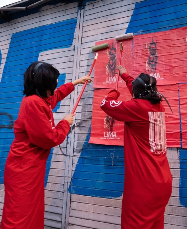 Two people dressed in red coveralls paste cryptic Slipknot posters onto a wall in Lima as part of a guerrilla street campaign.