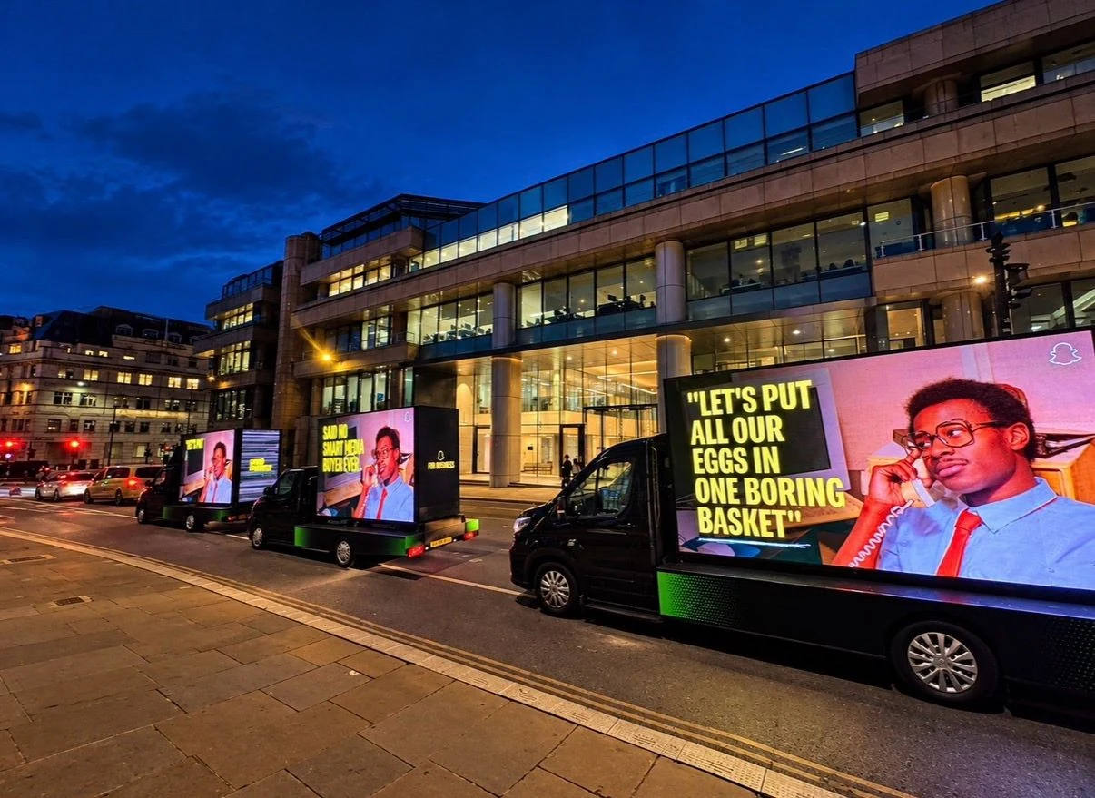 Snapchat mobile digital billboard vans driving through central London at night, showing the Spend Smarter campaign and the line Let's put all our eggs in one boring basket.