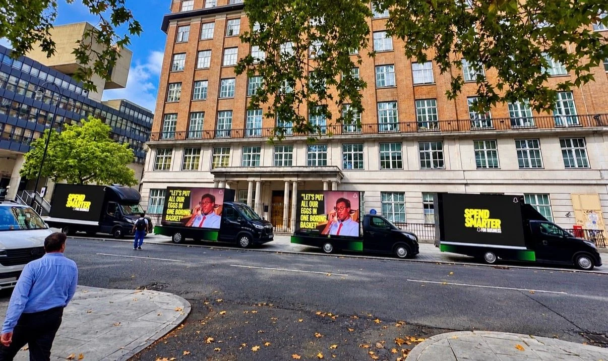 Four black Snapchat mobile digital billboard vans parked along a London street, displaying the yellow Spend Smarter message and a creative reading Let's put all our eggs in one boring basket.