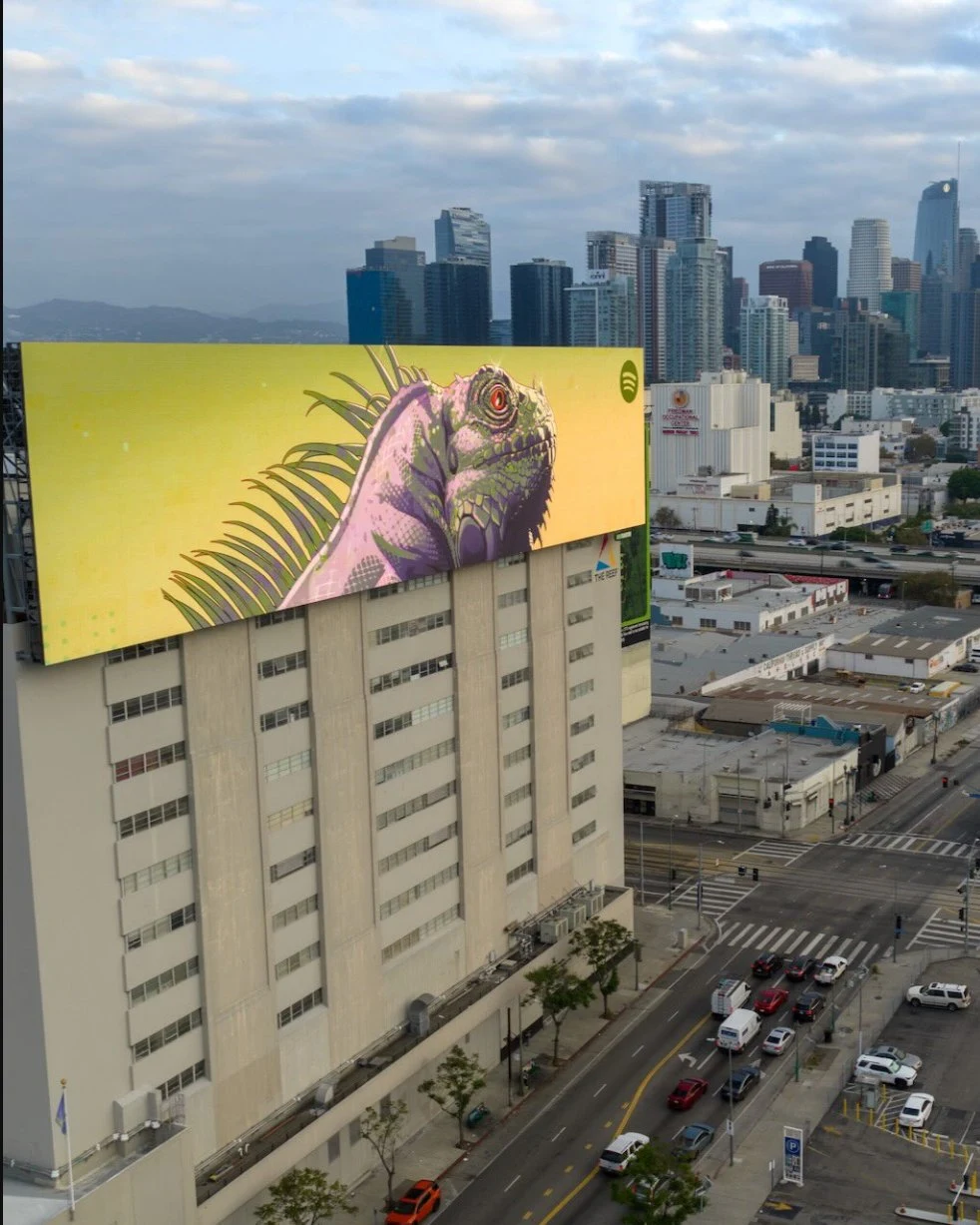 Massive Spotify-branded GTA VI-style billboard in Los Angeles showing a colorful iguana against a yellow background with the Los Angeles skyline behind it.