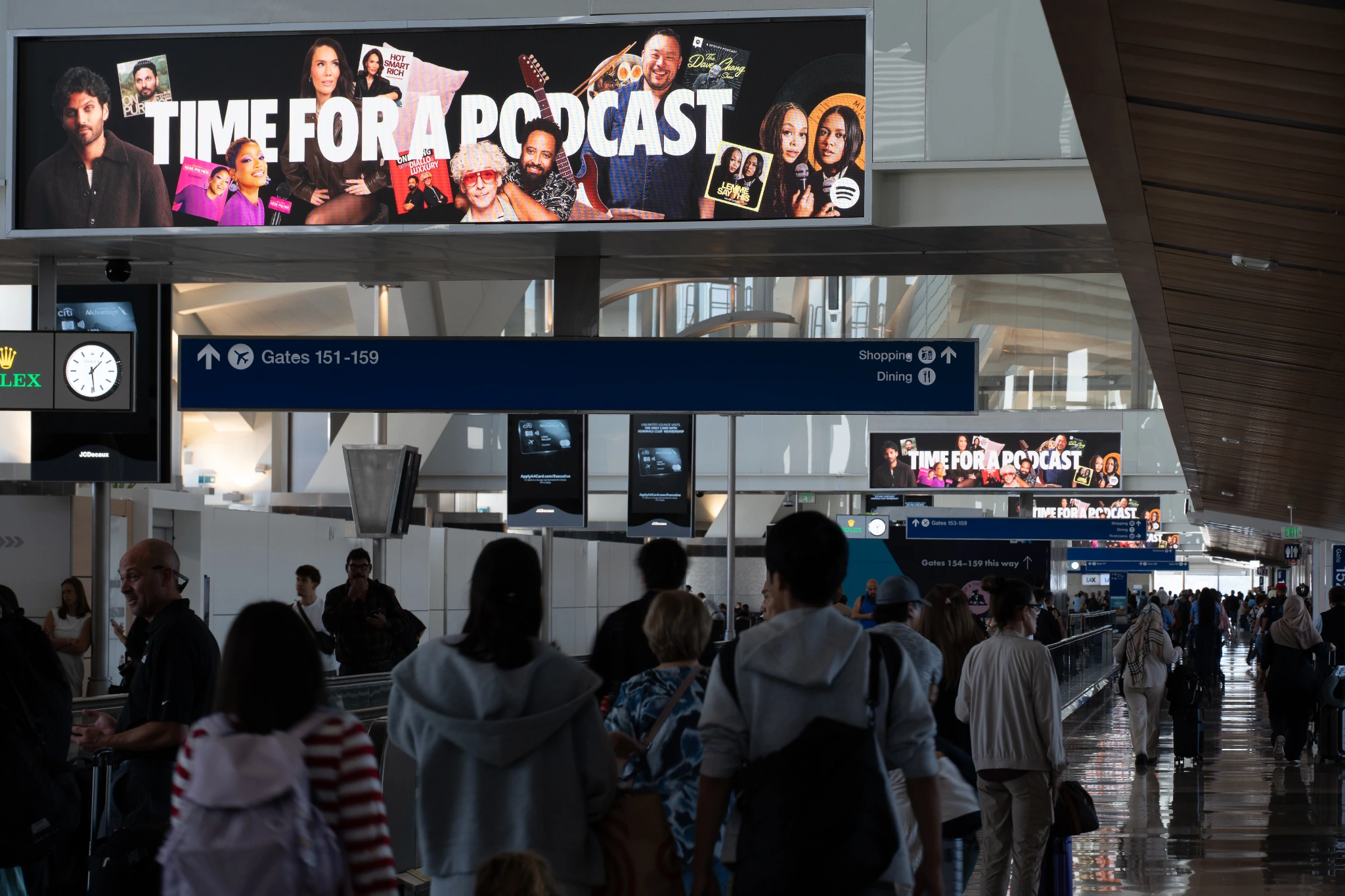 Spotify airport DOOH campaign displaying the message Time for a Podcast across multiple digital screens in a busy terminal.