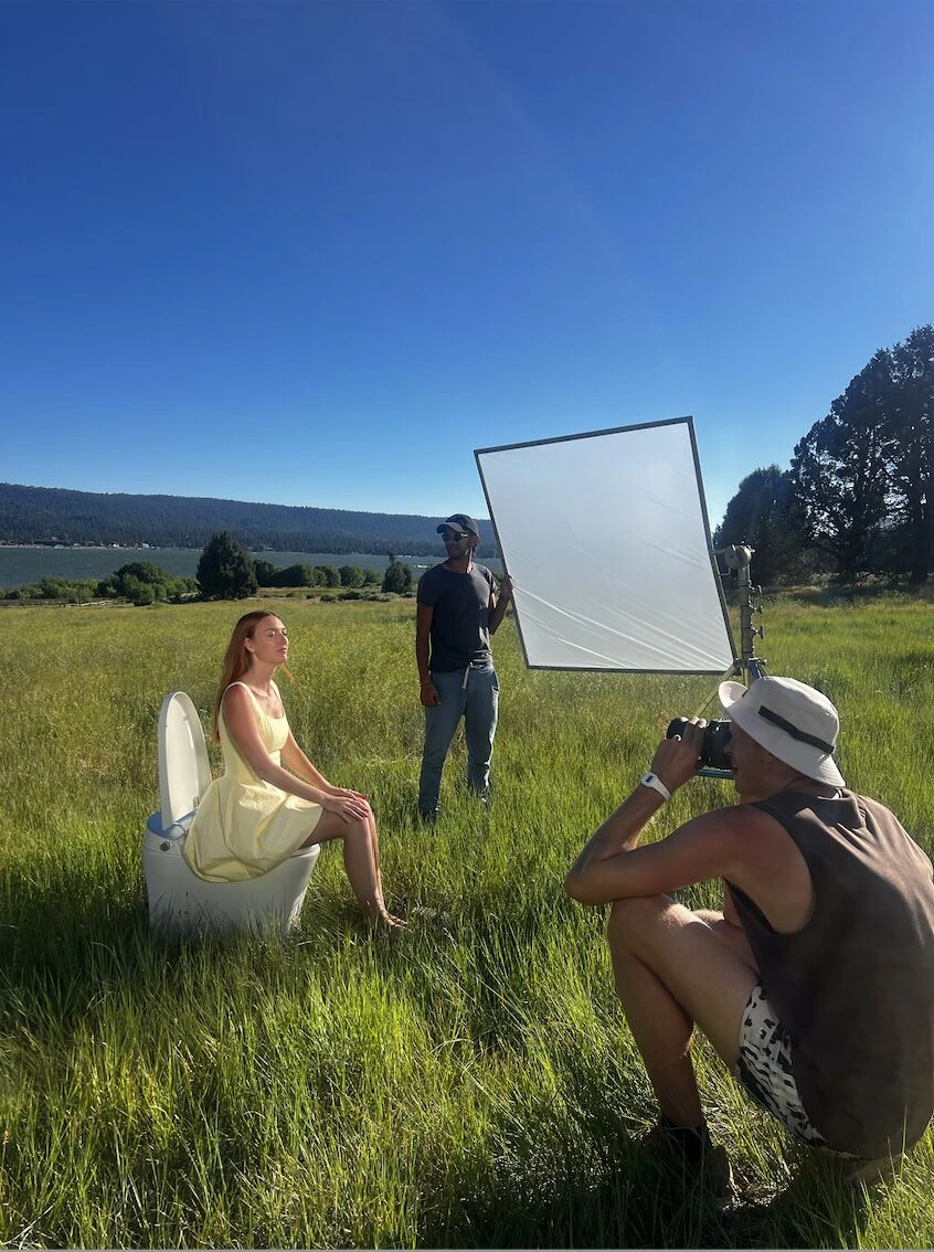 Behind-the-scenes TUSHY campaign photo shoot in a grassy field at Big Bear Lake with a model sitting on a toilet.