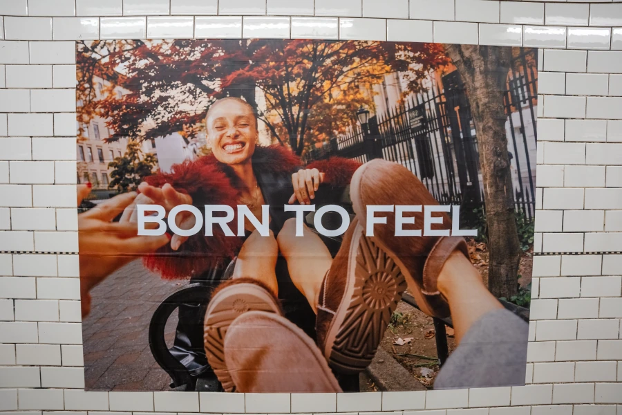 UGG Born To Feel poster in a New York subway station featuring boots and fall lifestyle imagery.