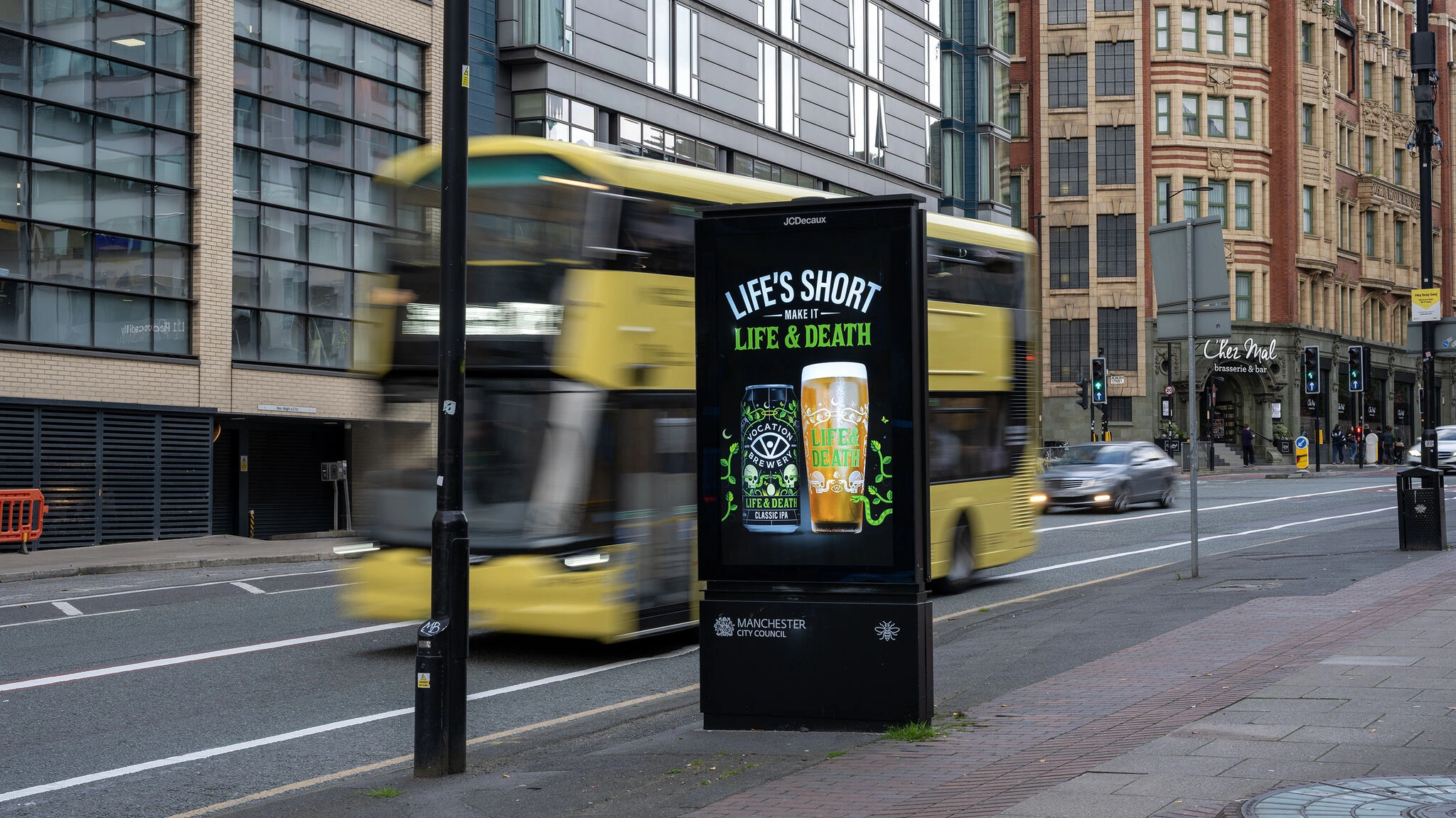 Life & Death IPA campaign creative displayed on a digital unit at a city crossing with buses and pedestrians moving past.