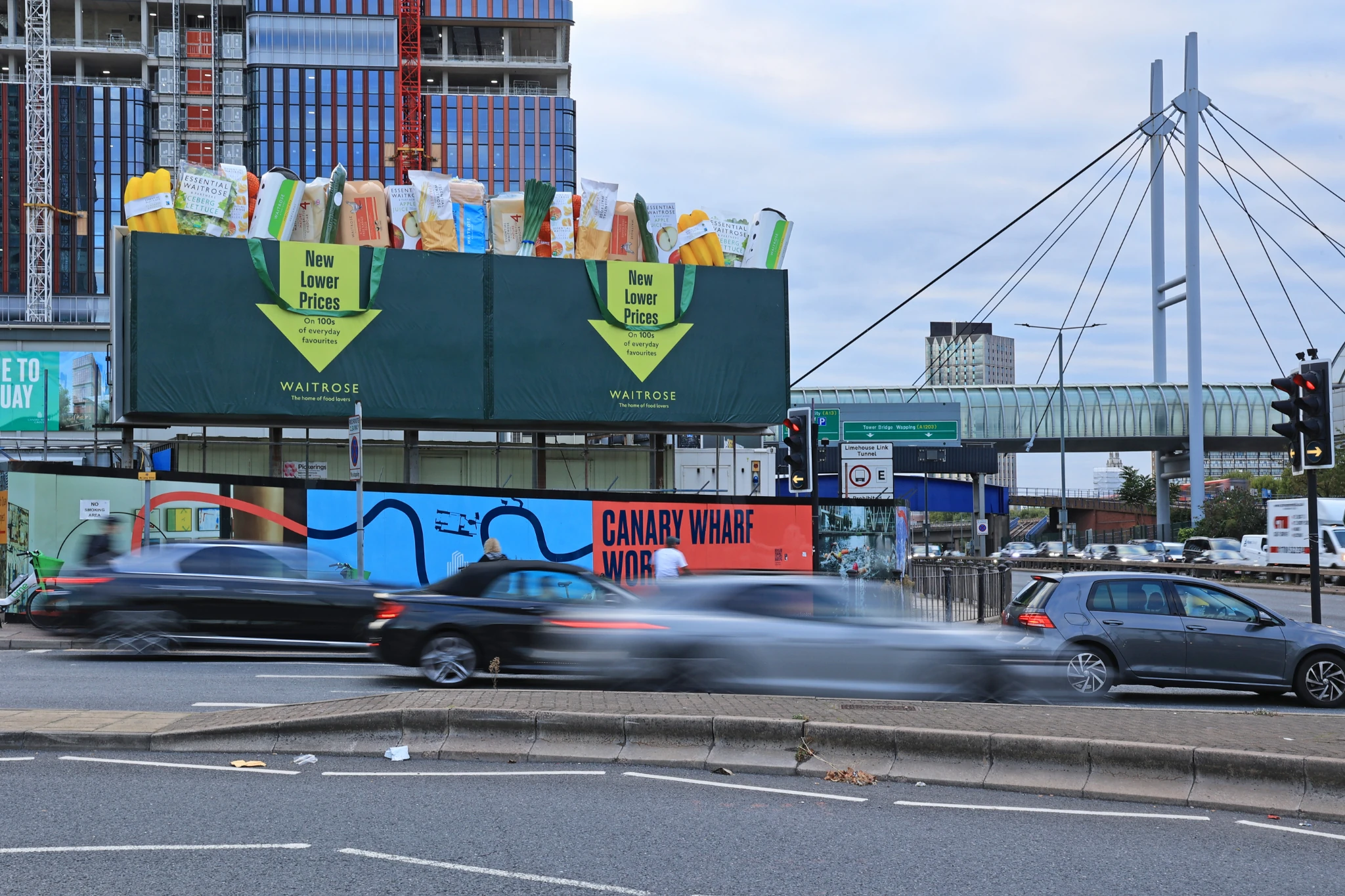 Waitrose special-build billboard in London featuring oversized shopping bags overflowing with everyday groceries to promote new lower prices.