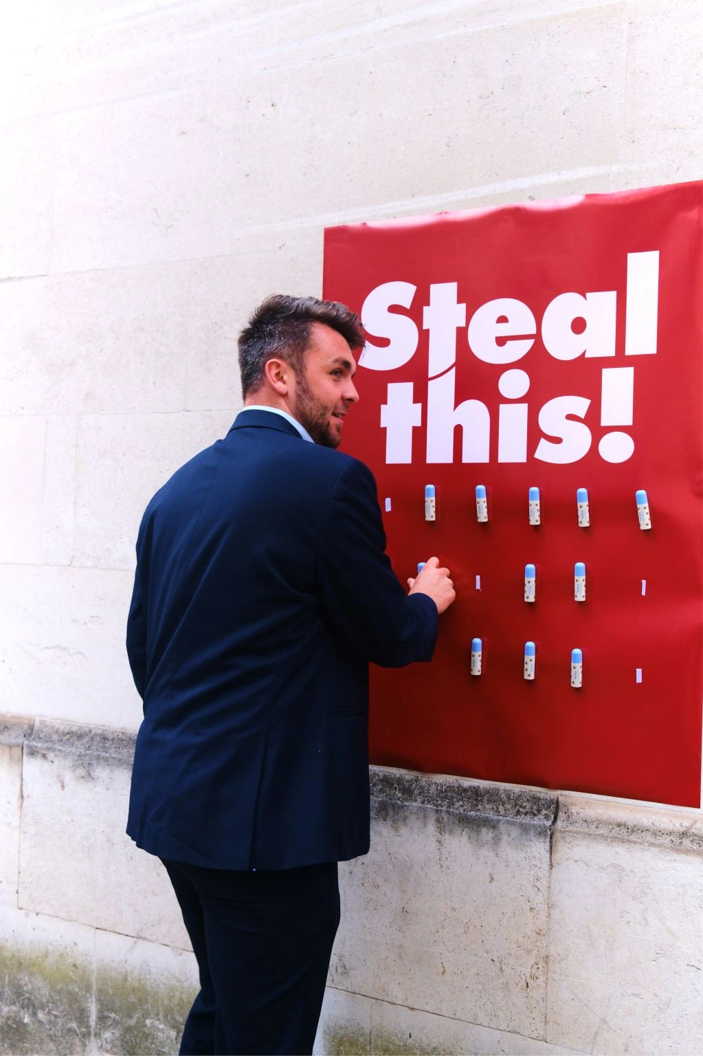 Close view of a suited passerby taking a Wild lip balm from the Steal this campaign poster.