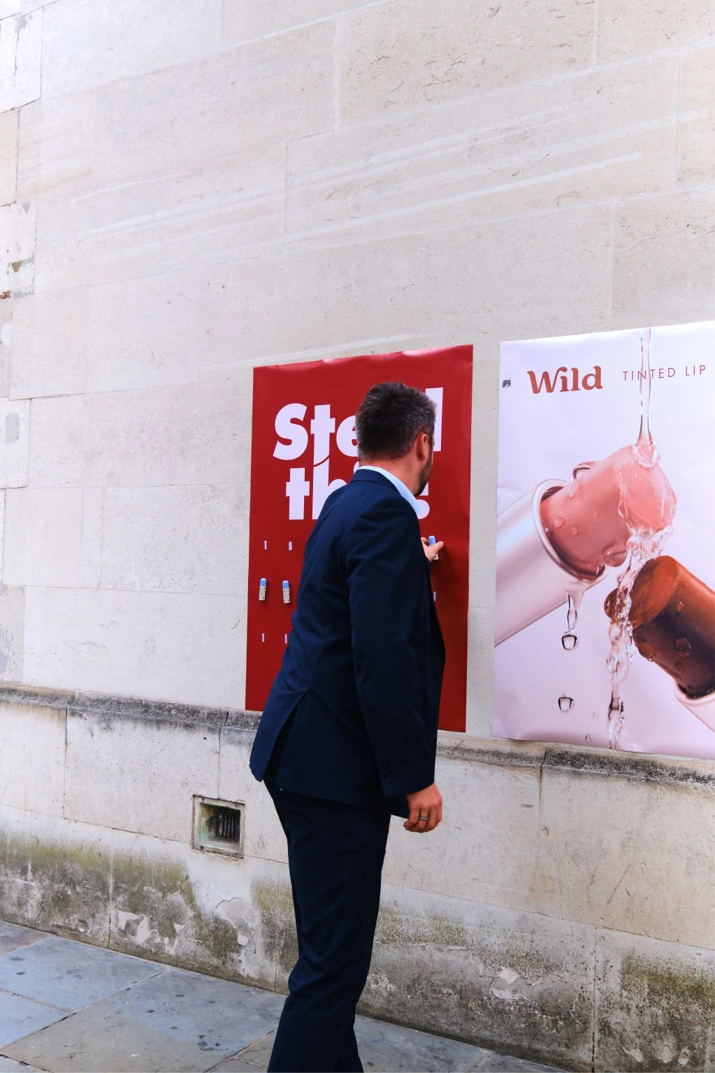 Man taking a Wild tinted lip balm from a Steal this street poster next to a Wild product poster.